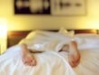 A person lying in bed with feet exposed under a white blanket, softly lit bedroom with warm lighting and abstract wall art.