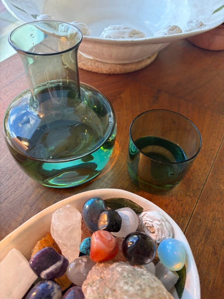 A calming tabletop arrangement with a glass carafe, bowl and a dish of crystals, creating a peaceful, grounding atmosphere in the treatment space.