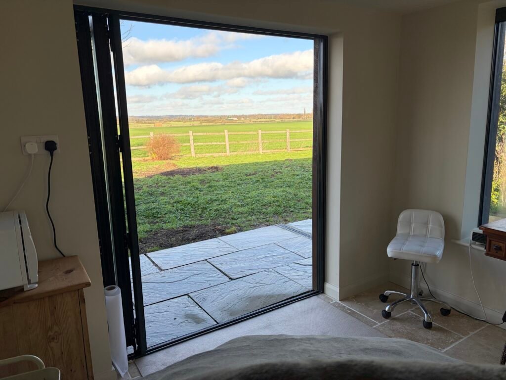 Alison Steyn’s tranquil garden room, with soft natural light and open countryside views designed to support relaxation and ease.