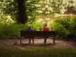 Two people sitting together on a bench beside a peaceful woodland pond.